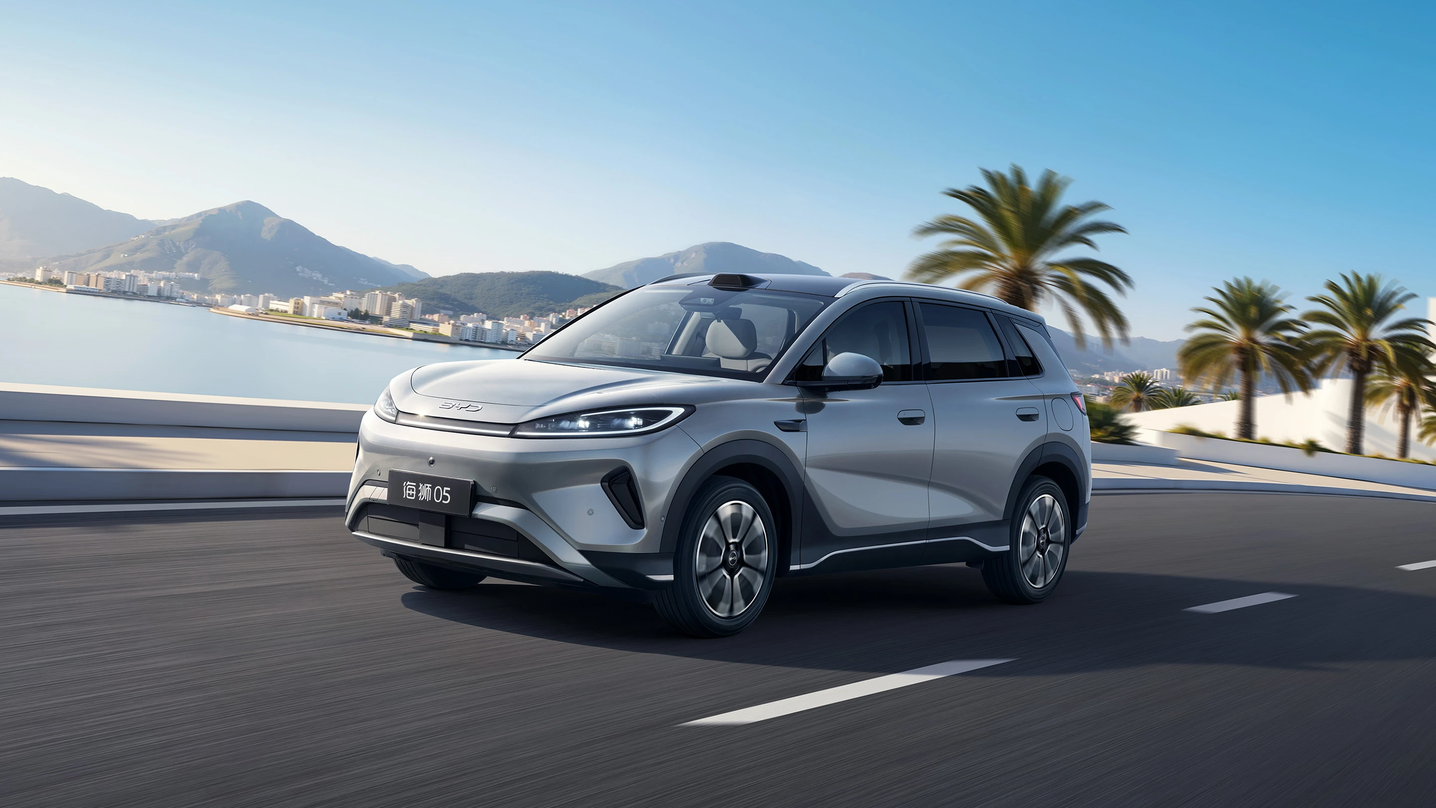 Berline électrique BYD Seagull modèle 2026, carrosserie argentée, prise sur une route côtière avec paysage montagneux en arrière-plan.