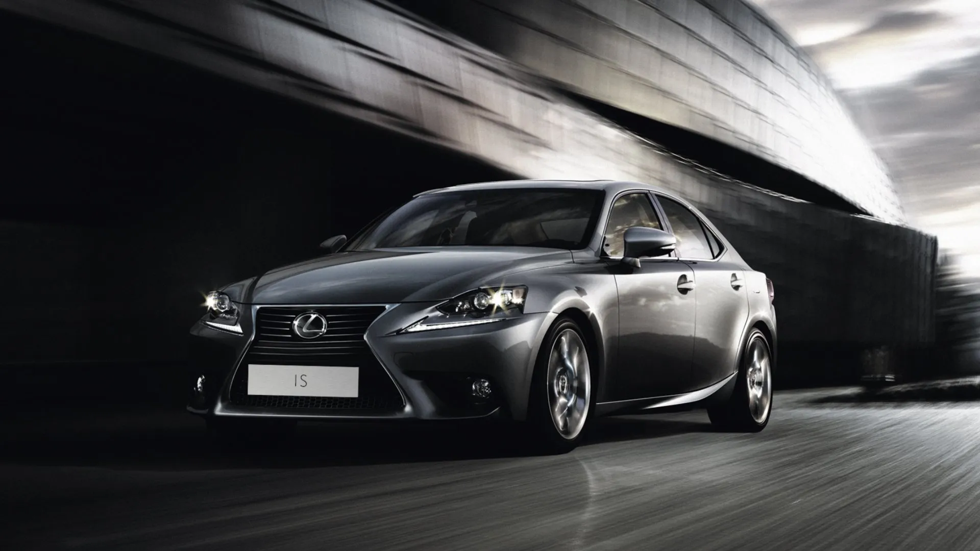 Vue avant latérale d'une berline Lexus IS de 2017 en gris foncé circulant sous un viaduc urbain