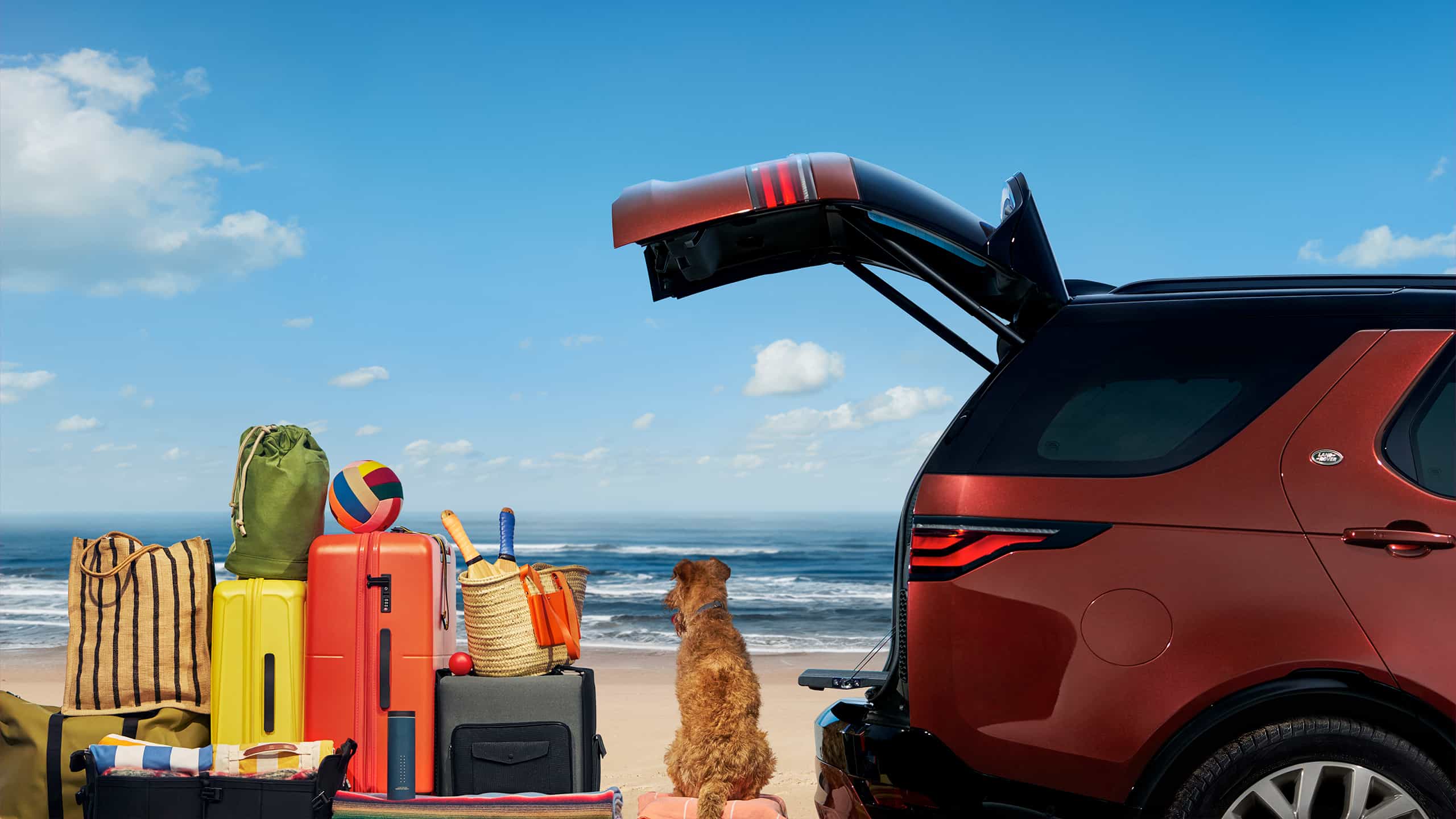 Vue arrière latérale de la Land RoverDiscovery 2026 en rouge, sur fond de plage