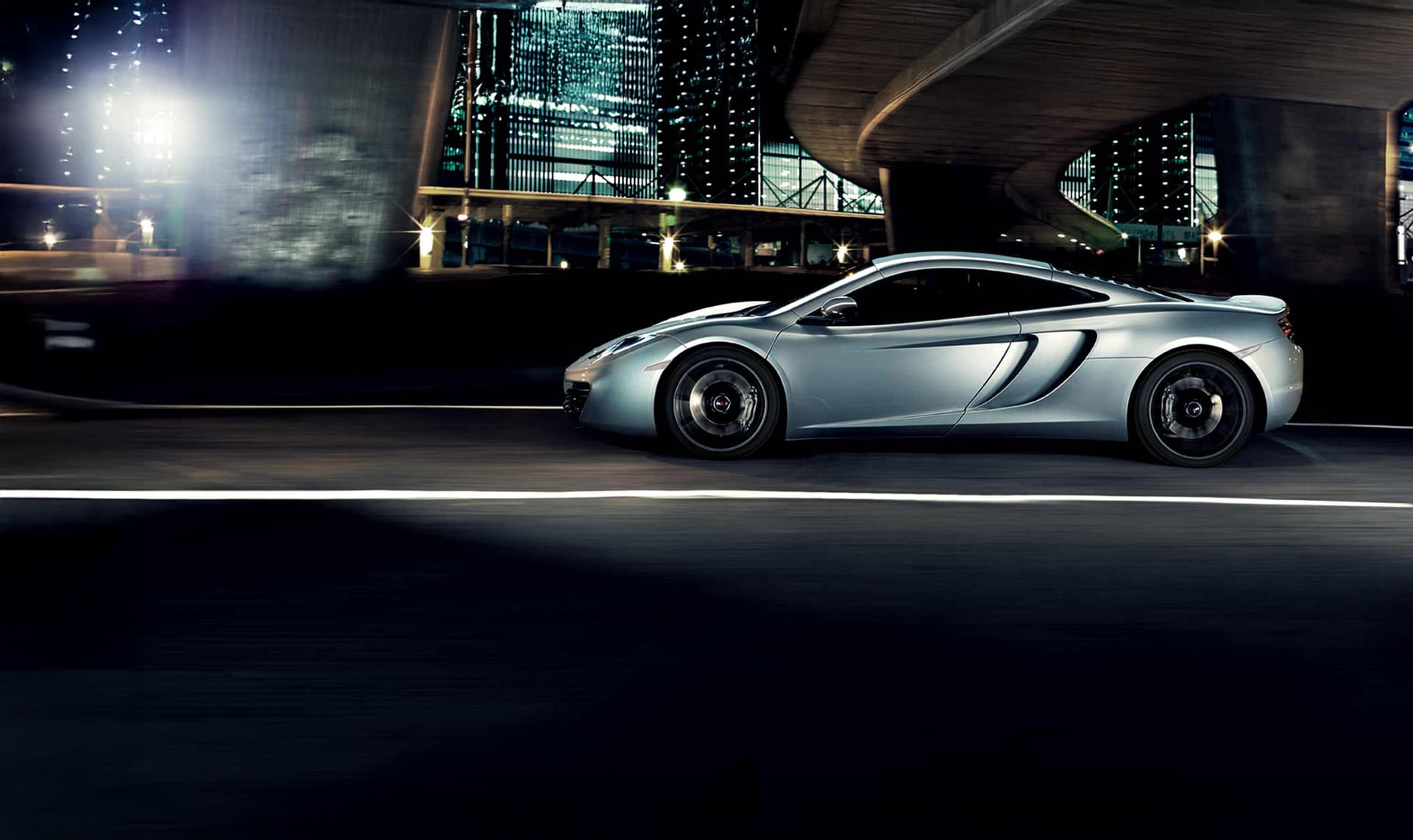 Dynamic right-side view of a 2011 McLaren 12C coupe in silver, against a TownCar night backdrop