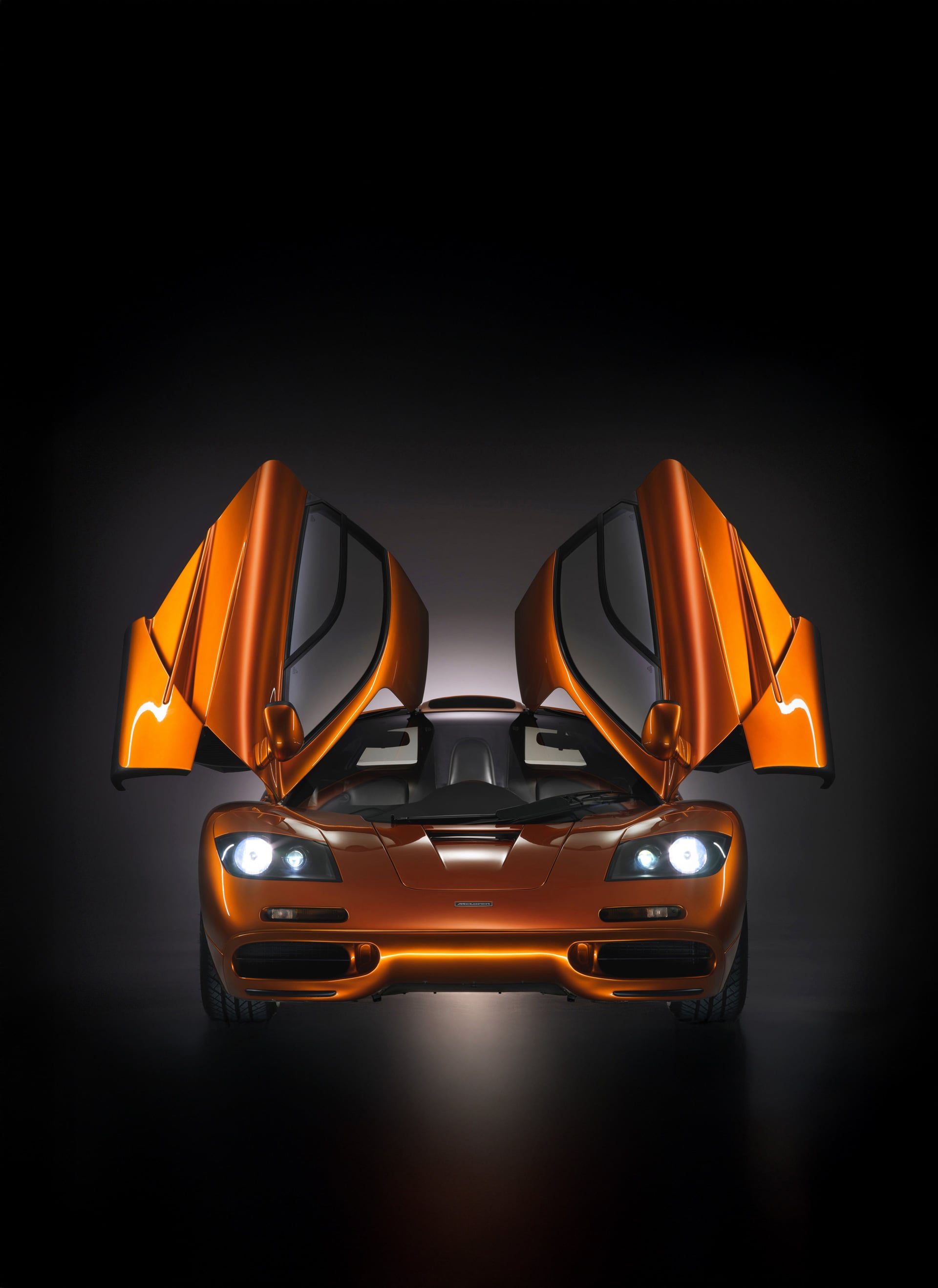 Orange McLaren F1 with upward-opening doors against a black background.