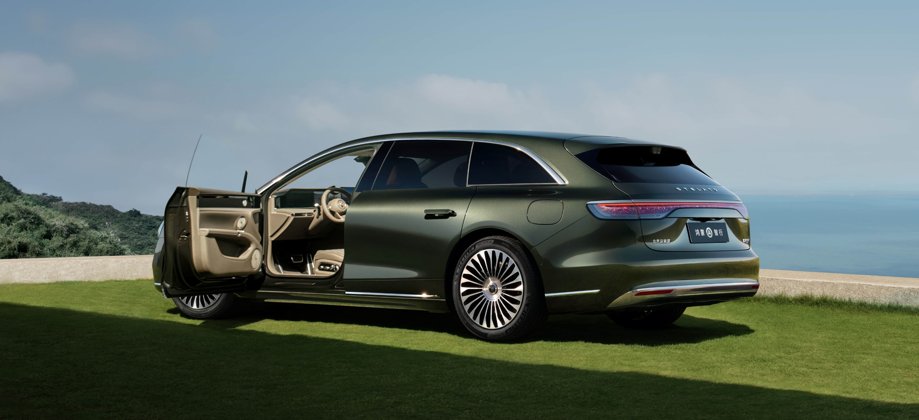 Forest-green STELATO STELATO S9T 2025 sedan, right-side view, set against grassland and ocean backdrop